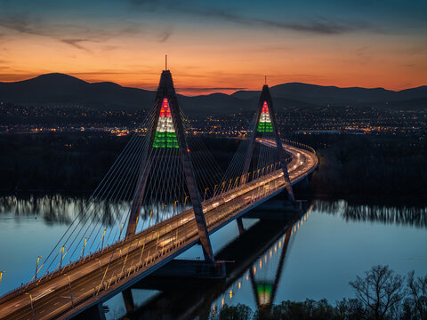 Budapest, Hungary - Aerial view of Megyeri Bridge illuminated in festive Hungarian national colors in honor of the 1848 March 15th Revolution and War of Independence at sunset with blue and golden sky