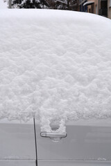 A silver passenger car is completely covered in a thick layer of fresh powdery snow with only the door handle visible.