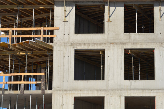 A concrete building facade under construction showing empty window frames and wooden scaffolding supports during a winter day.