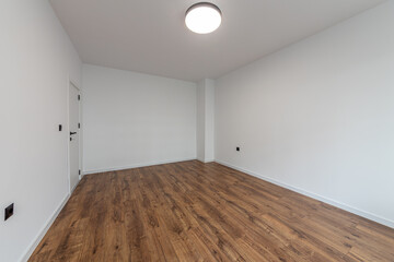 Laminated wood floor with white wall. Empty room with floating laminate in new apartment. Home renovation and real estate background.