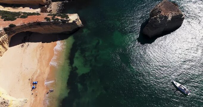 Aerial drone view of beach with dinghy and yacht near Benagil sea caves, Algarve Portugal, cinematic commercial grading