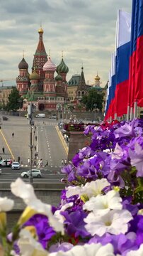 RUSSIA, MOSCOW - June 13, 2025: The Moscow Kremlin with Russian flags fluttering in the wind on a cloudy day, and bright flowers in the flowerbeds. The tricolor is framed by St. Basil's Cathedral. 4К