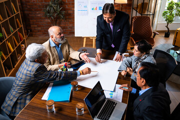 Senior Indian Asian executives reviewing plans and drawings together at modern office desk