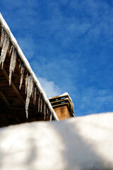 Smoke rising from a house chimney on a snowy roof in winter