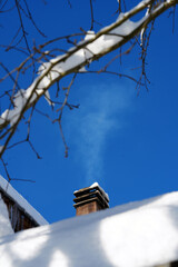 Smoke rising from a house chimney on a snowy roof in winter