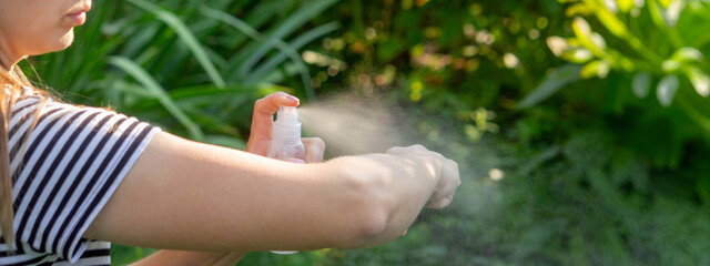 Obraz premium Woman applying protective spray on her arm in the garden. Insect repellent or sunscreen