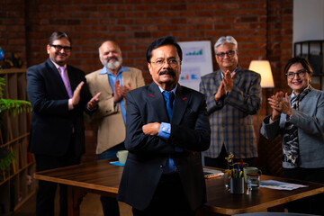 Senior Indian male executive smiling at camera with colleague standing in modern office