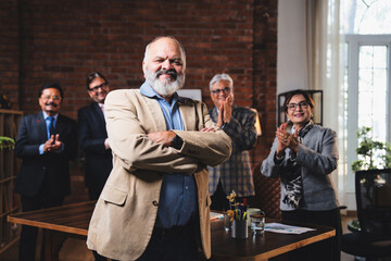 Senior Indian male executive smiling at camera with colleague standing in modern office