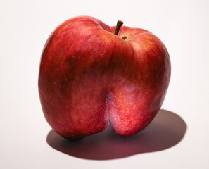 An ugly red apple. A fruit with a shape flaw on a white background.