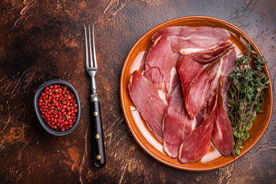Balkan Prsut prshut, sliced cured pork meat ham on plate. brown background. top view