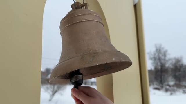  Hand Ringing Large Brass Bell in Outdoor Setting.Close-up image of a hand ringing a large brass bell outside. The bell is prominently displayed, with the hand gripping the clapper. 