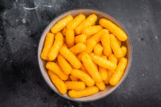 Deliciously addictive cheese flavored corn puffs, beautifully arranged on a plate. black background. top view