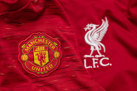 Close-up of Manchester United and Liverpool FC embroidered crests on red football jerseys, symbolizing classic English Premier League rivalry.