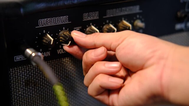 Close-up musician hands plugging guitar cable into amplifier.