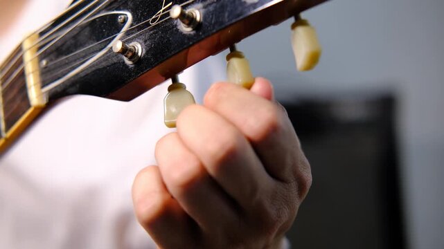 Hand of guitarist tuning electric guitar strings, music preparation