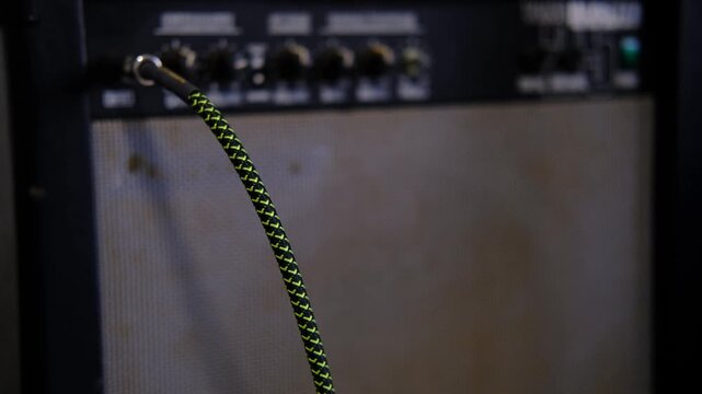 Close-up hand turning volume knob and plugging guitar cable during amplifier setup.