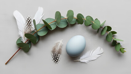 Easter decorations with blue egg, eucalyptus branch, and feathers on gray background. Minimalist design features pastel palette, muted colors, and natural elements.