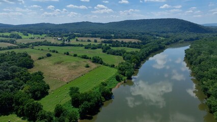 Peaceful green fields and farmland beside Potomac River in Virginia with mountains and cloud reflections in water on summer day 