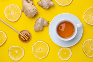 Cup of tea with honey and ginger surrounded by lemon slices on a yellow surface
