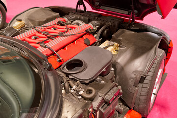 Close view of a car engine with red detailing on display at a car exhibition in a bright venue during the weekend
