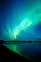 Northern lights dancing over calm lake in Farnebofjarden national park in north of Sweden.
