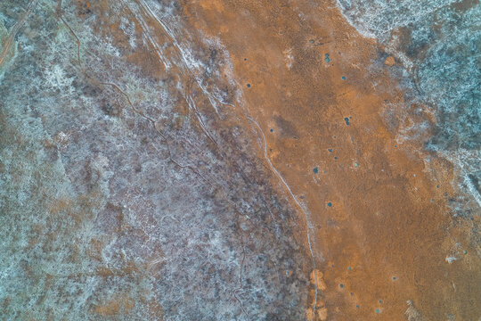 Winter marshland surface with frozen soil and dry vegetation patterns resembling alien planet aerial drone shot
