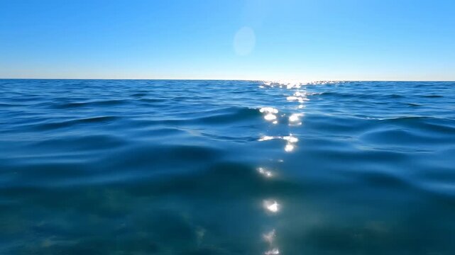 Calm ocean surface shimmers underneath a cloudless blue sky
