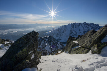 View of jagged, snow-dusted peaks rise majestically against the crisp blue sky, rocks with patches of green moss, sun shining brightly, Vysoke Tatry, Presov Region, Slovakia.