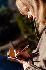Close up of woman journaling and reflecting on new year intentions on sunny terrace. Mindfulness,...