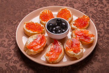 Canap s with red caviar and trout on a plate with olives on a brown tablecloth