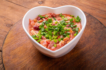 Heart-shaped salad with chicken and beans on a round wooden stand