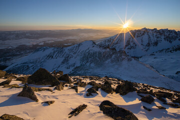 View of the sun bursts forth over snow-laden peaks, casting a golden glow on the rugged rocks in Koncista, Vysoke Tatry, Presov Region, Slovakia.