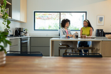 Diverse female friends chatting and sipping coffee at modern kitchen island with ceramic mugs