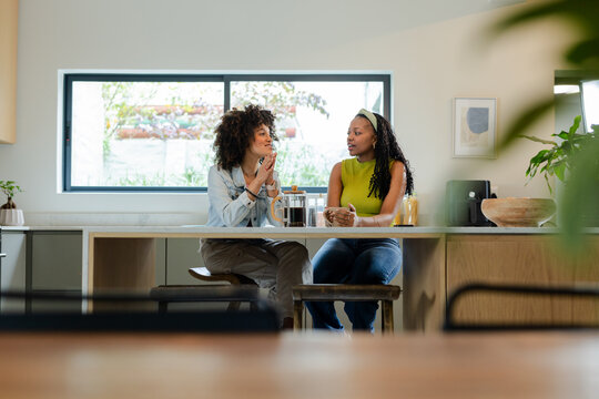 Diverse female friends holding coffee mugs, chatting at kitchen island with French press