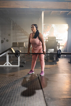 Mid-30s African American woman lifting loaded barbell in gym on rubber flooring wearing pink outfit
