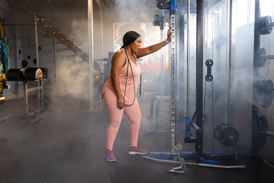 African American woman standing in pink athletic set by cable machine with weight stack, jump rope