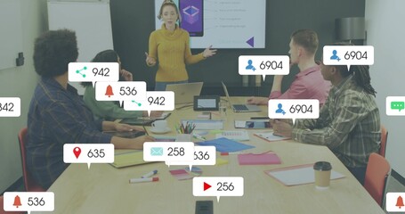 Presenting woman in mustard sweater explaining slide in boardroom, with laptops and alert icons