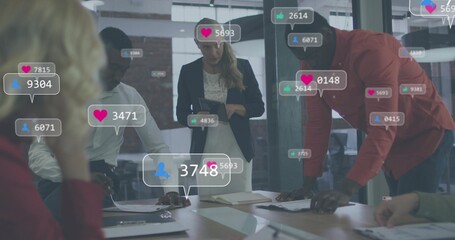 Four colleagues leaning at table in office, viewing tablet and social metrics, wearing dark blazer