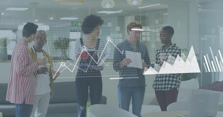 Five coworkers wearing jackets reviewing projected data on glass wall in open office, with tablets