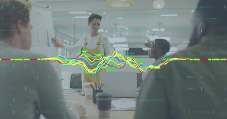 Presenting male in mustard overalls pointing at whiteboard in meeting, with laptop and coffee cups