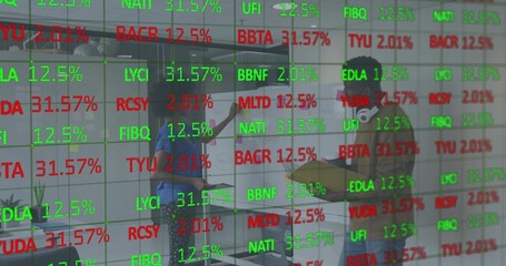 Pointing coworkers in casual clothes discussing work in office, with glass wall showing tickers