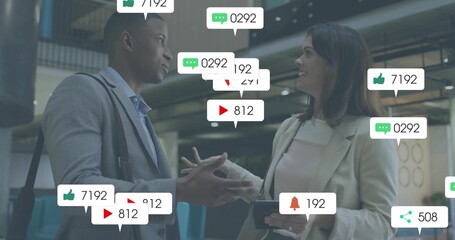 Discussing colleagues in lobby, gray suit and light blazer holding tablet, shoulder bag with alerts