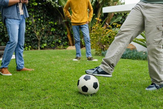 Three male friends practicing soccer on yard near cones, right man controlling ball in cargo pants
