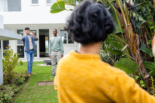 Male friends chatting on backyard lawn by modern white house, foreground wearing mustard sweater