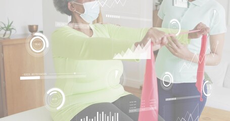 Guiding caregiver assisting seated senior performing arm exercise at home with red band and masks