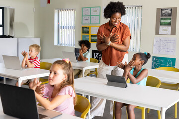 African American teacher guiding school-age students at school using laptops and tablet, copy space