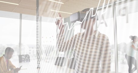 Pointing woman wearing VR headset and striped shirt reaching toward glass wall in office, tablet