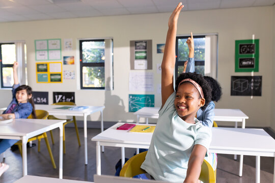 Diverse class raising hands in class African American child sitting at desk with notes, copy space