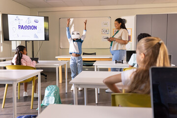 African American teacher with device guiding class, male student wearing VR at front PASSION screen