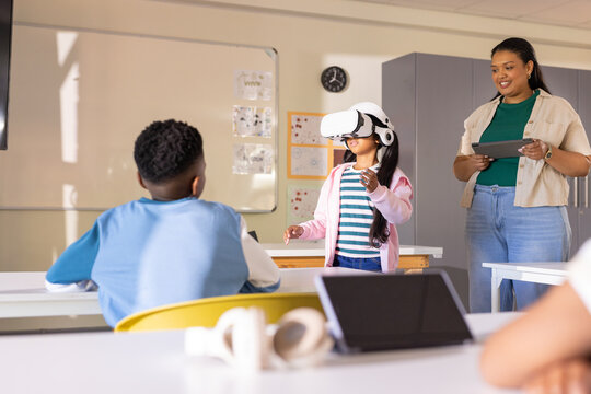 African American teacher with tablet guiding youth interacting in VR headset in class, copy space